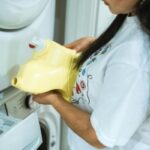 A Woman in White T shirt Holding Yellow Plastic Bottle Near a Washing Machine 2