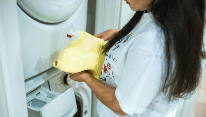 A Woman in White T shirt Holding Yellow Plastic Bottle Near a Washing Machine 2